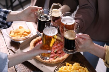 Friends clinking glasses of beer at table, closeup
