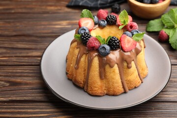 Tasty Bundt cake with berries, chocolate and mint on wooden table, closeup