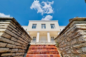 Geometric centered frame with a building, stone walls and a cloud above.