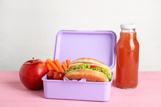 Open lunch box with delicious food and juice on pink wooden table against light grey background