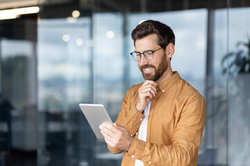 Fototapeta premium Man using a tablet in a modern office space with a thoughtful expression