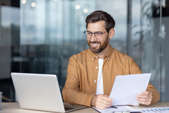 Businessman reviewing documents while working at his laptop in a modern office