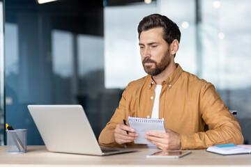 Focused man working on laptop and writing notes in a modern office