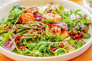 Shrimp salad with various vegetables, close-up on a wooden dining table
