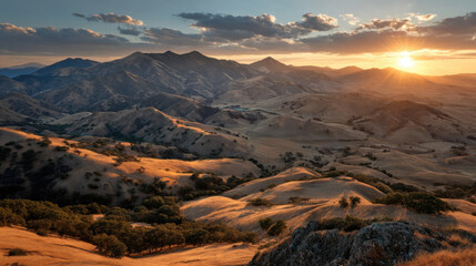 Obraz premium Breathtaking sunset over rolling hills and mountains, showcasing golden grasslands and dramatic clouds. serene landscape evokes sense of peace and natural beauty