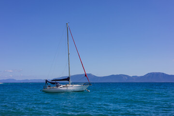 Fototapeta premium A sailing yacht in a calm sea against a backdrop of rocky shores in the rays of bright summer sun. Peaceful seascape. Adriatic Sea, Croatia.