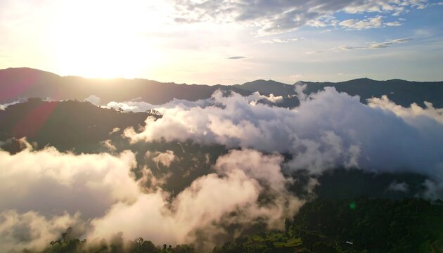 A breathtaking aerial view of a mountain range enveloped in a sea of clouds at sunrise, showcasing the dramatic contrast between the sunlit peaks and the misty valleys below.