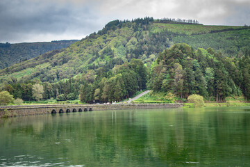 A beautiful lake with a bridge and trees in the background. The water is calm and the sky is cloudy
