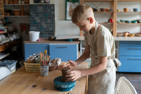 Smiling boy shaping clay at pottery workshop table