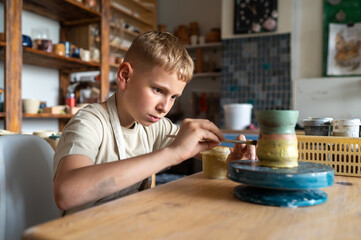 Fototapeta premium Focused boy painting ceramic cup at home pottery studio