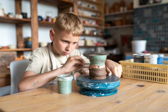 Focused boy painting ceramic cup at home pottery studio
