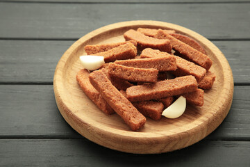 Tasty rye croutons on wooden plate on black background.