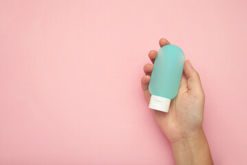 Hand holding blank blue plastic tube on pink background. Cosmetic beauty product branding mockup.