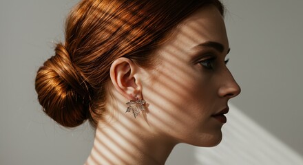 Red-haired woman with make-up, portrait side view, wearing earrings in shape of maple leaf. Neutral background with sun rays. Symbolic accessories of autumn or fall and Canada Day jewelry