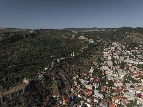 Aerial view of the Kartlis Deda statue standing tall amid lush greenery, contrasting with the red-roofed buildings of the city, Tbilisi, Tbilisi, Georgia.