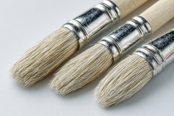 Three paintbrushes with wooden handles and silver ferrules on a white surface, arranged close together.