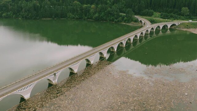 Aerial view of Bicaz Lake Bridge crossing calm waters with forested hills and mountains