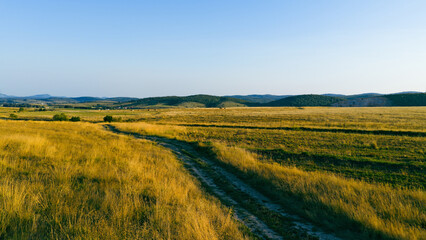 Rural trail across sunlit steppe landscape with distant hills on the horizon