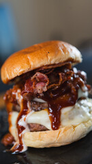 Massive gourmet burger with two juicy beef patties, overflowing melted cheese, crispy bacon, rich bacon mayo, and special sauce on a toasted brioche bun. Extreme food close-up