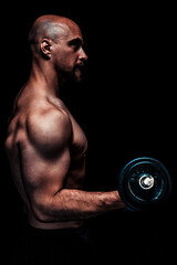 Profile of shirtless muscular man performing bicep curl with dumbbell