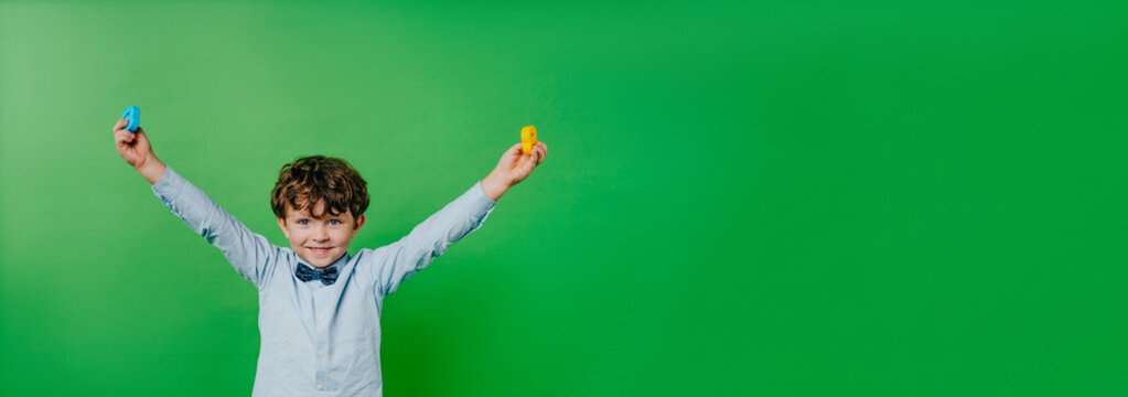 Happy preschool boy wearing bow tie holding number toys standing over green background