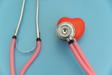 Pink stethoscope with red heart on blue background, cardiologist's instruments