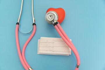 Pink stethoscope with red heart with cardiogram tape on blue background, cardiologist's instruments