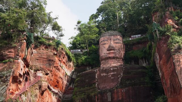 Slow motion centered framing of Buddha&rsquo;s head and torso with dramatic light and background foliage in Leshan, Sichuan