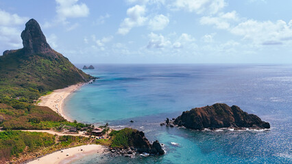 Drone sobre a Praia da Conceição, destacando mar turquesa, areia clara e o imponente Morro do Pico compondo cenário tropical preservado de Noronha