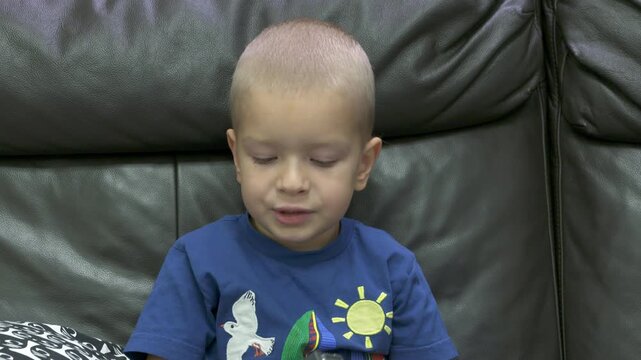 Child playing with new toy sitting on sofa at home. Concentrated face of little boy holding transformer robot toy. Three year old child examining new toy comments on his actions.