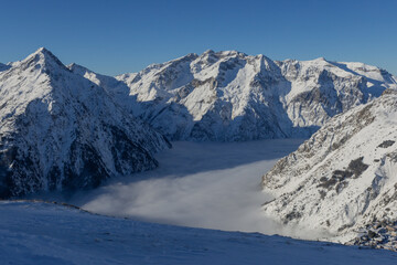 Naklejka premium Snowy mountains rise above a blanket of cloud that cover valley