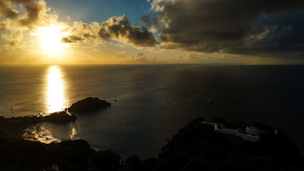 Fototapeta premium Pôr do sol dourado sobre a região costeira de Fernando de Noronha visto de cima, criando atmosfera paradisíaca única.