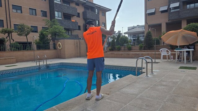 Worker maintaining residential swimming pool in a modern urban setting. Lifeguard cleaning the pool in the urbanization