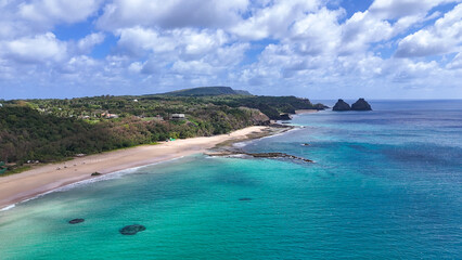Visão aérea da Praia do Americano em Noronha com mar azul e Morro Dois Irmãos ao fundo, cenário paradisíaco e preservado