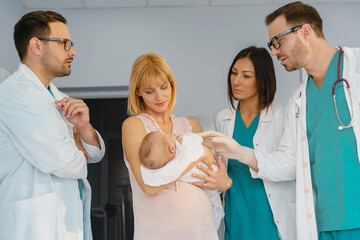 Fototapeta premium New Mom Cradling Baby and Engaging with Medical Team in Bright and Supportive Hospital Environment