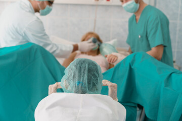 Healthcare Professionals In Scrubs Working Together During Childbirth Procedure In Hospital Delivery Room