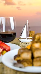 A model sailboat sits on a table amidst food and drinks at sunset.