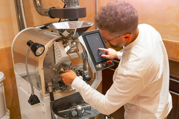 A worker is focused on the roasting machine, skillfully managing the process of preparing arabica and robusta coffee beans in a workshop setting with various coffee equipment