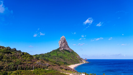 Imagem aérea do Morro do Pico e da costa de Fernando de Noronha, mostrando falésias, mar azul profundo e vegetação verde, símbolo da natureza exuberante e preservada da ilha © RNL Fotografia