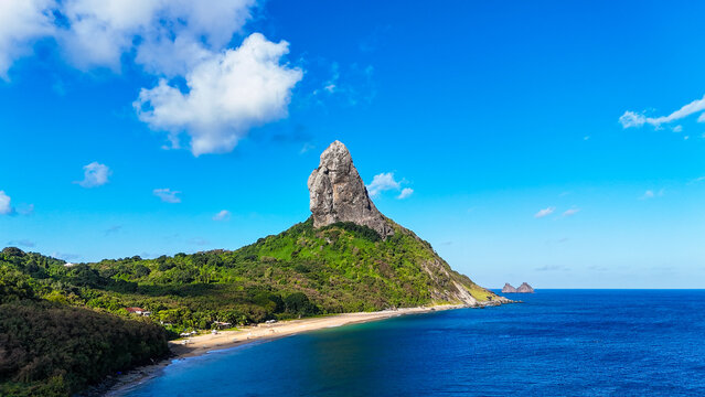 Morro do Pico iluminado pelo sol, com o mar cristalino ao redor e vegeta&ccedil;&atilde;o caracter&iacute;stica da ilha de Fernando de Noronha.