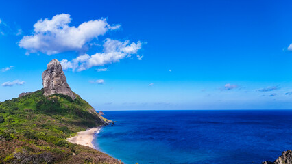 Panorama aéreo da orla de Fernando de Noronha com o mar azul e falésias, exibindo a harmonia entre o oceano e a vegetação tropical da ilha, ícone do turismo ecológico. © RNL Fotografia