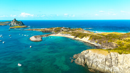 Vista aérea deslumbrante da Praia do Porto em Fernando de Noronha, ondas quebrando nas pedras, pôr do sol dourado refletindo no mar, cenário tropical perfeito para relaxar e contemplar