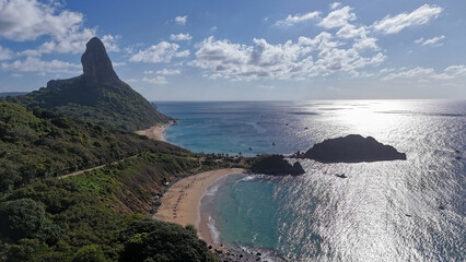 Vista aérea da orla de Fernando de Noronha com mar azul e falésias, refletindo a beleza natural, o turismo sustentável e o equilíbrio entre mar e vegetação tropical. © RNL Fotografia