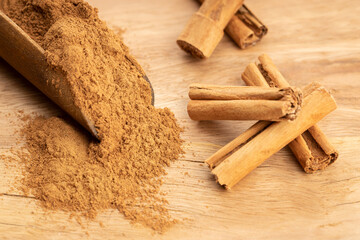 Cinnamon powder and cinnamon sticks in wooden scoop on wooden table. Close up