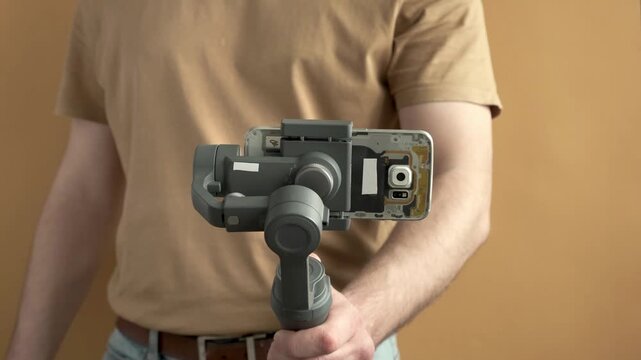 Man filming with a smartphone using a gimbal stabilizer on yellow background. Using three-axis electronic stabilizer to make vlogs or video shooting.