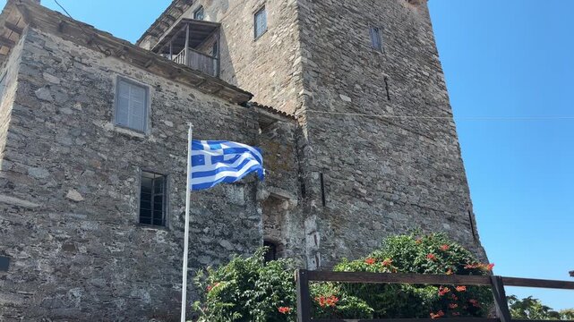 Medieval Ouranoupoli Tower with Greek flag, located at the gateway to Mount Athos, under clear blue summer sky.