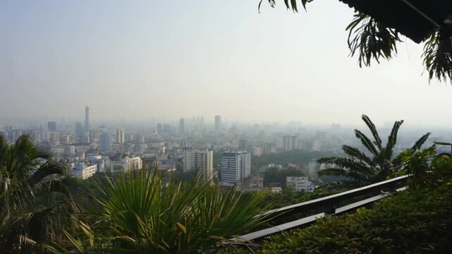 Panoramic view of a city skyline with lush greenery in the foreground and hazy background