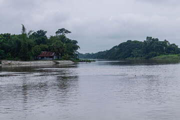 Peaceful flowing river bordered by lush forest and solitary riverside house in distance.