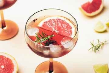 Close up of grapefruit cocktail with ice cubes and rosemary in glass on beige background. Closeup