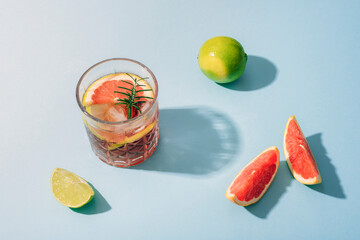 Glass of grapefruit cocktail with lime slices and rosemary on blue background with sharp shadows. Top view